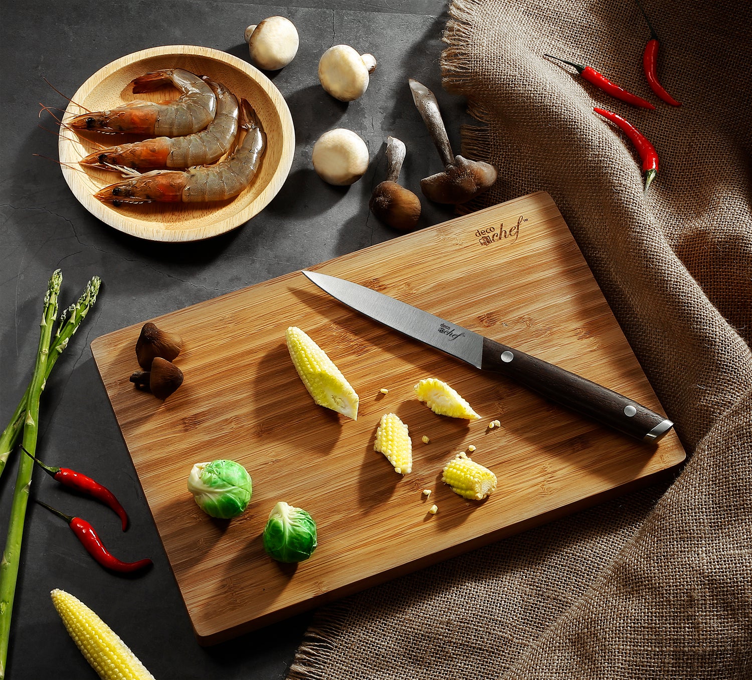 Knife sitting on cutting board in a dark background with various vegetables